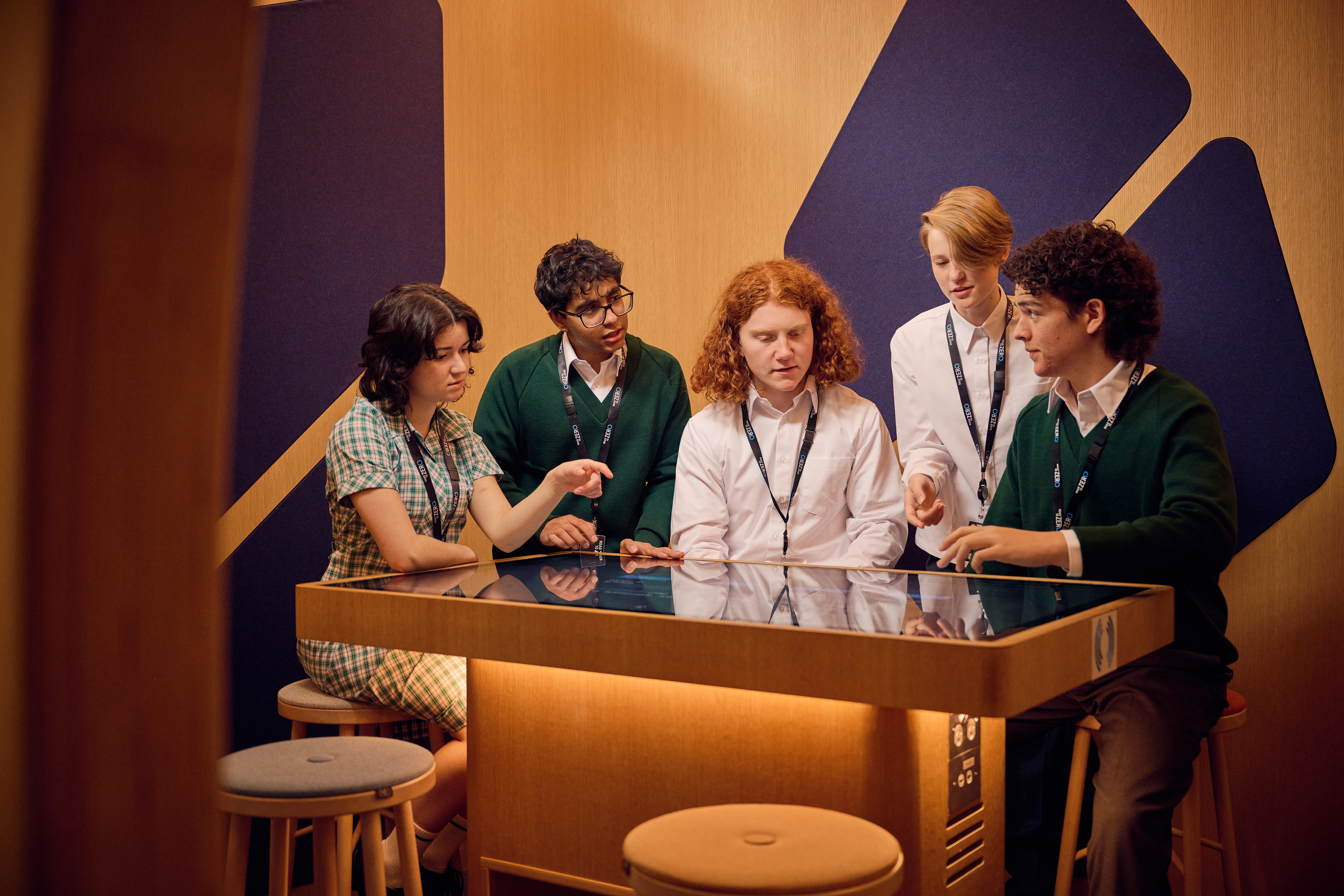 A group of teenage students discuss what's on a table screen in front of them