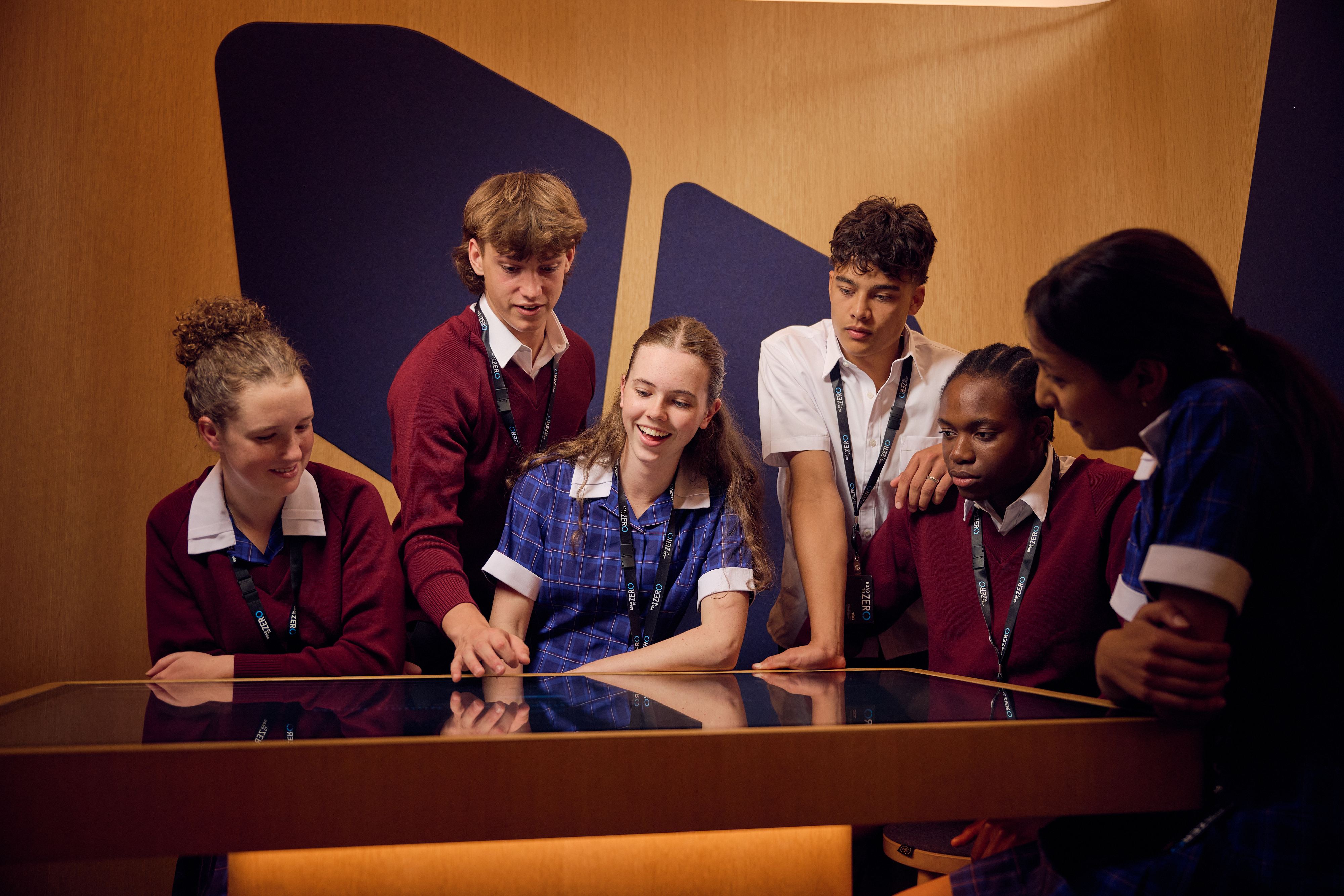 A group of teenage students interact with a table screen